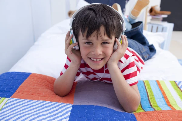 Smiling boy listening to music in bed with headphones on — Stock Photo, Image