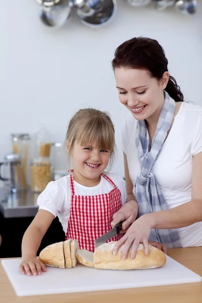 Mutter lehrt Tochter, wie man Brot schneidet — Stockfoto