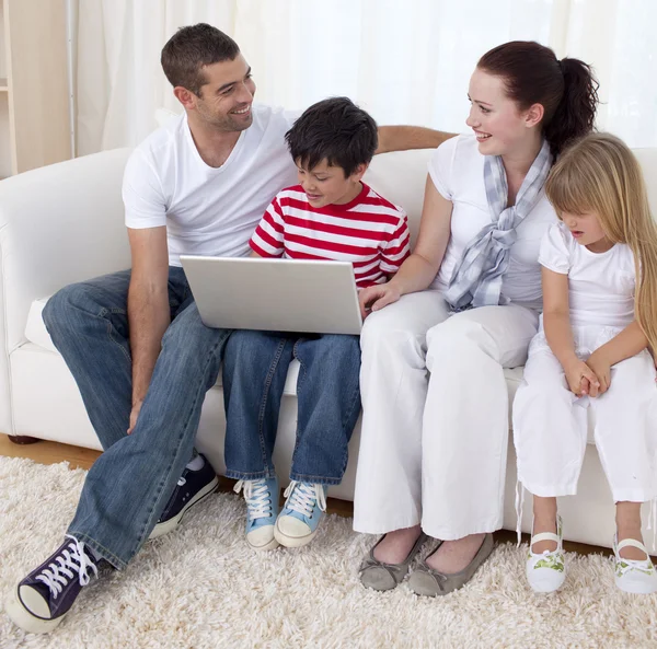 Familia sonriente en la sala de estar usando una computadora portátil — Foto de Stock