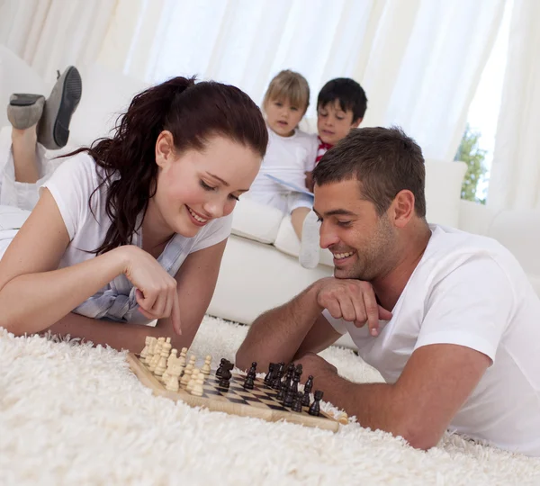 Casal sorridente jogando xadrez no chão na sala de estar — Fotografia de Stock