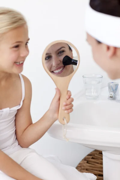 Χαμογελώντας κόρη κρατώντας ένα καθρέφτη και μητέρα βάζοντας μακιγιάζ — Φωτογραφία Αρχείου
