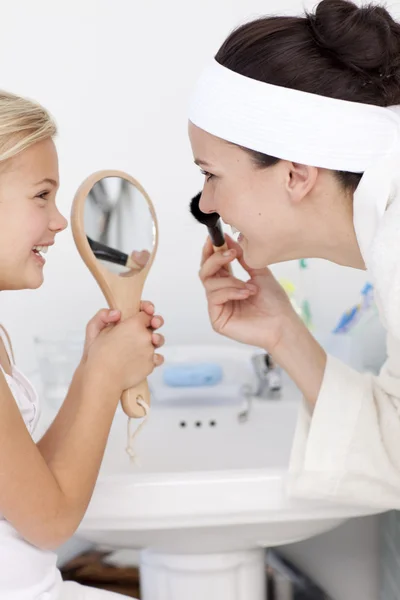 Filha segurando um espelho e mãe colocando maquiagem — Fotografia de Stock