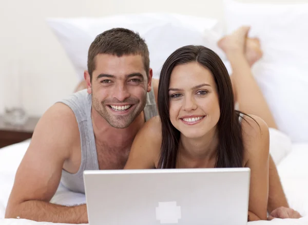 Улыбающаяся пара в постели с помощью ноутбука — стоковое фото