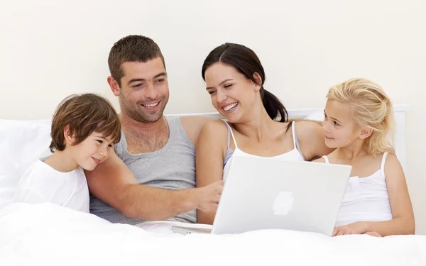 Föräldrar och barn använder en bärbar dator i sängen — Stockfoto
