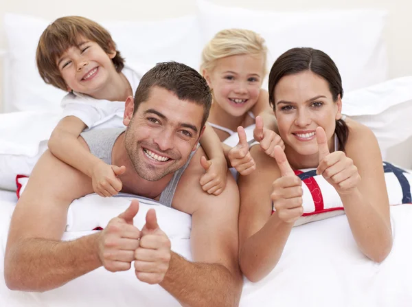 Family playing in bed with thumbs up — Stock Photo, Image