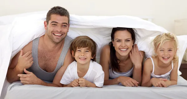 Pais e filhos brincando na cama dos pais — Fotografia de Stock
