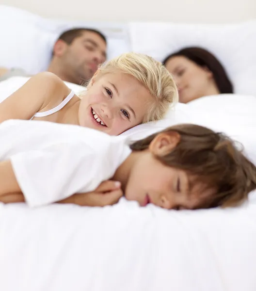 Niña sonriendo en la cama mientras su familia duerme —  Fotos de Stock