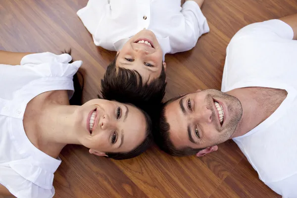 Parents and kid lying on floor with heads together — Stock Photo, Image