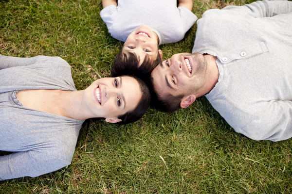 Pais e criança deitados no jardim com as cabeças juntas — Fotografia de Stock