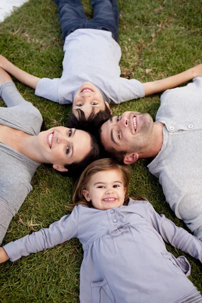 Família deitada em um jardim com cabeças juntas — Fotografia de Stock