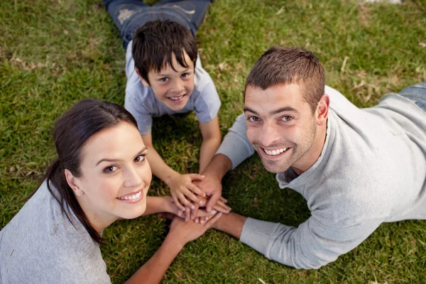 Parents and kid lying on garden with hands together — Stock Photo, Image