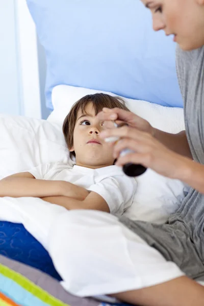 Mother giving her son lying in bed syrup — Stock Photo, Image