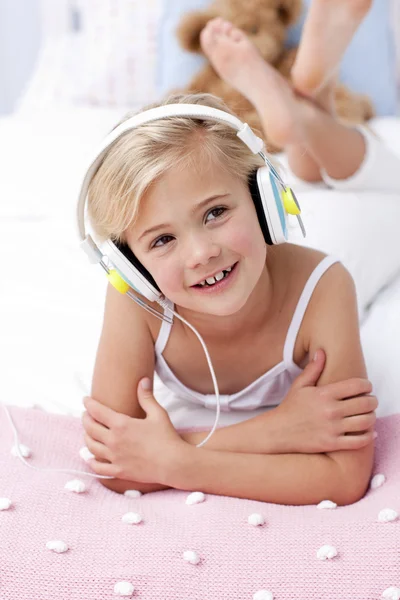 Маленька дівчинка слухає музику в ліжку з навушниками — стокове фото