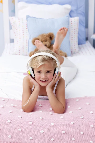 Uśmiechnięta dziewczynka leżąc w łóżku słuchając muzyki — Zdjęcie stockowe