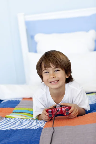 Улыбающийся мальчик играет в видеоигры в своей спальне — стоковое фото