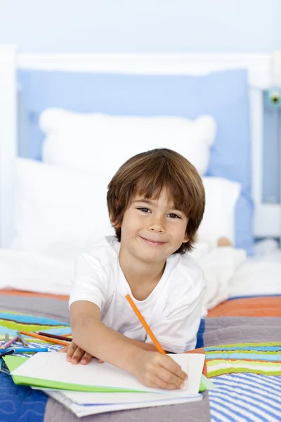Усміхнений маленький хлопчик малює в ліжку — стокове фото