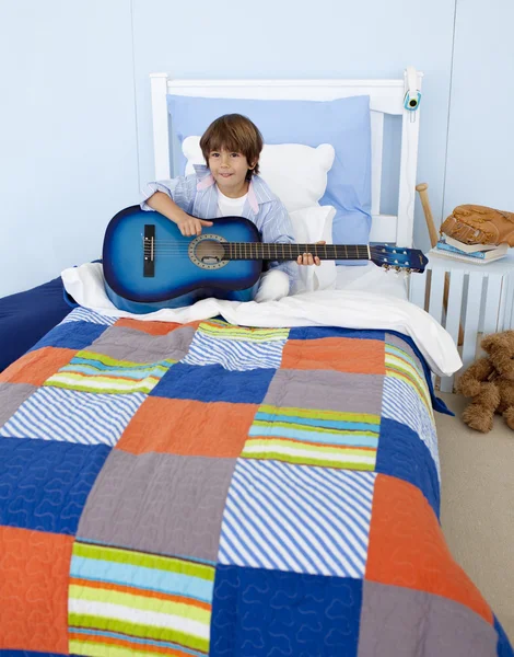 Mały chłopiec gra na gitarze w sypialni — Zdjęcie stockowe