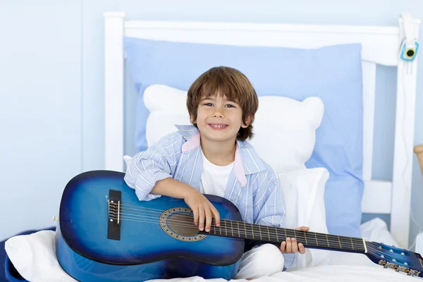 Happy little boy playing guitar in bed — Stock Photo, Image
