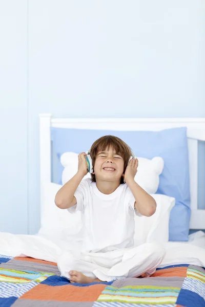 stock image Little boy listening to music on headphones in his bed