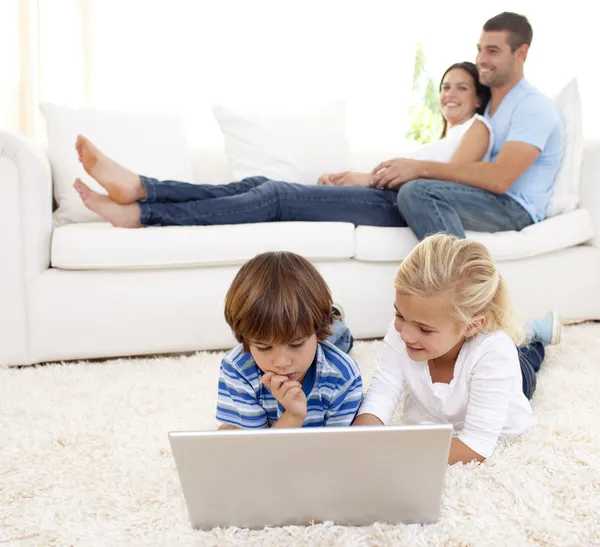 Дети с ноутбуком и родителями, лежащими на диване — стоковое фото
