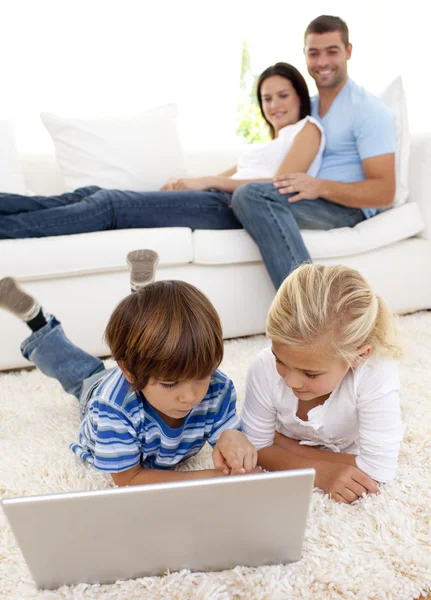 Niños usando una computadora portátil y una pareja tumbada en el sofá —  Fotos de Stock