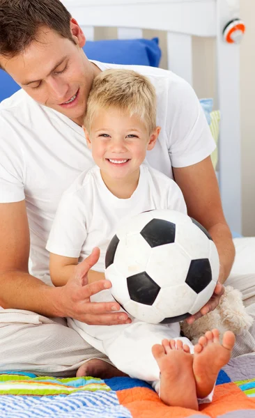 Улыбающийся мальчик и его отец играют в футбол Стоковая Картинка