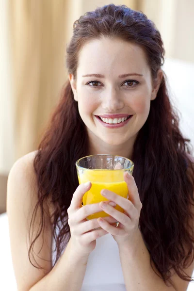 Smiling woman drinking orange juice in bedroom Stock Photo