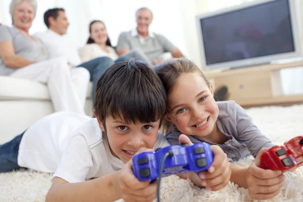 Bambini che giocano ai videogiochi sul pavimento e la famiglia sul divano — Foto Stock