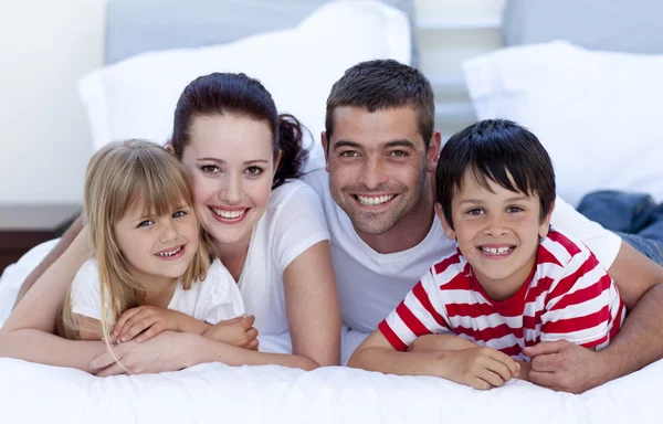 Lächelnde Familie liegt zusammen im Bett Stockbild