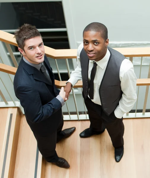 Dos hombres de negocios estrechando las manos en las escaleras y sonriendo a la cámara —  Fotos de Stock