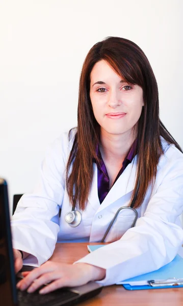 Morena médico usando um laptop e sorrindo para a câmera — Fotografia de Stock