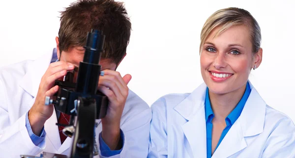 Mujer sonriendo a la cámara y científico masculino mirando a través de un — Foto de Stock