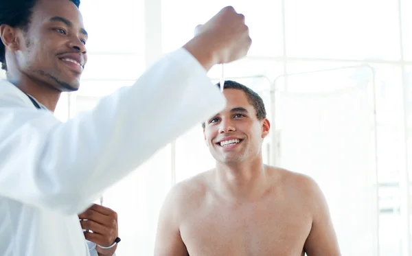 Médico sorridente verificando a temperatura do paciente masculino — Fotografia de Stock