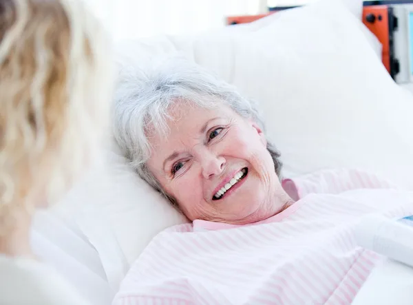 Mujer mayor sonriente acostada en una cama de hospital hablando con su gr —  Fotos de Stock