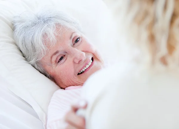 Веселая пожилая женщина лежит на больничной койке и разговаривает с ней — стоковое фото