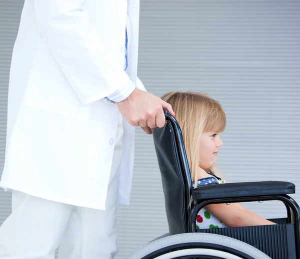 Küçük kız bir doktor tarafından desteklenen tekerlekli sandalye üzerinde oturan gülümsüyor — Stok fotoğraf