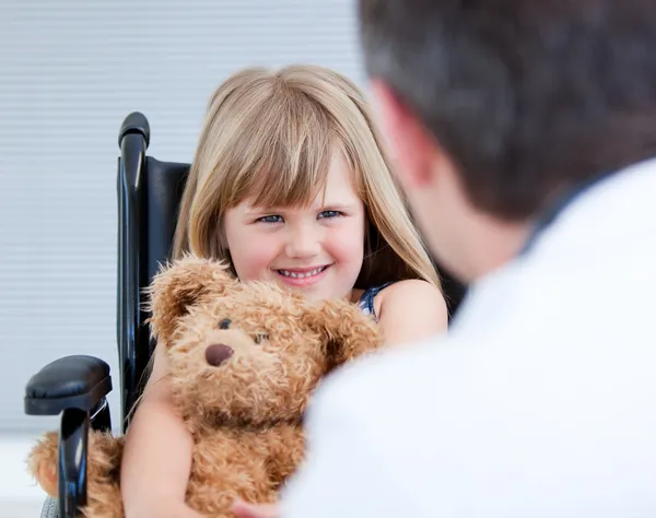 Lachende meisje, zittend op de rolstoel met haar teddy bea — Stockfoto