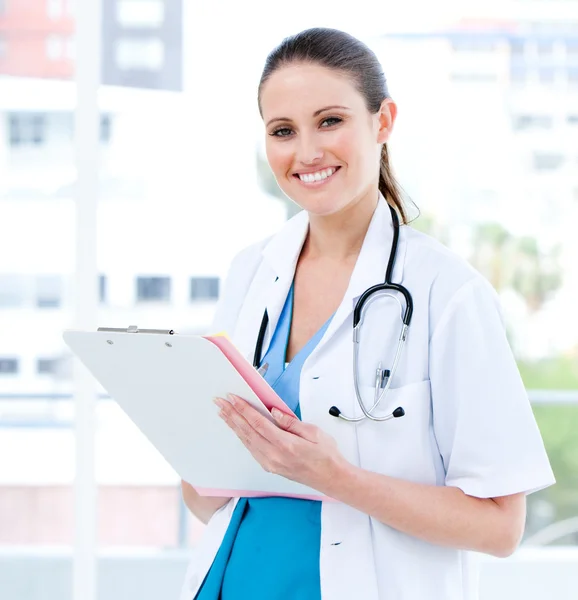 Happy female doctor writing her diagnosis looking at the camera — Stock Photo, Image