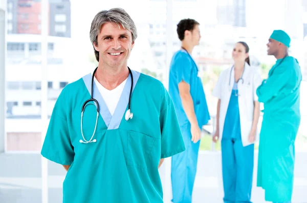 Glædelig mandlig doktor kigger på kameraet, mens hans medicinske partner - Stock-foto