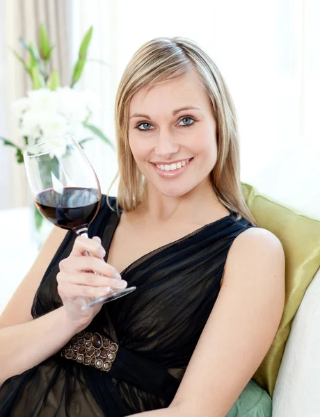 Красивая женщина сушит красное вино сидя на диване — стоковое фото