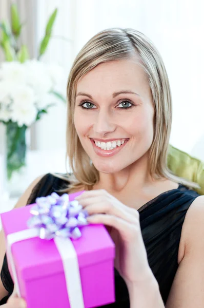 Glödande kvinna öppnar en gåva som sitter på en soffa — Stockfoto