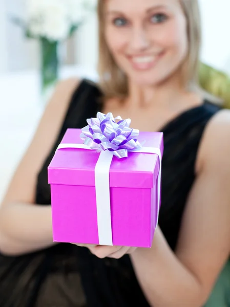 Blond žena otevírá dárek sedí na pohovce — Stock fotografie
