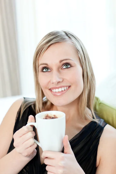 Stralende vrouw drinken een kopje koffie zittend op een bank — Stockfoto