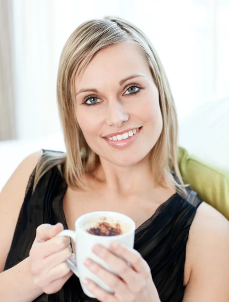 Bright woman drinking a coffee sitting on a sofa — Stock Photo, Image