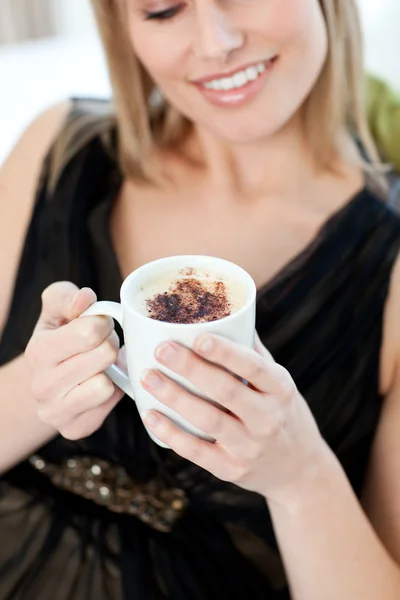 Blond woman drinking a coffee sitting on a sofa — Stock Photo, Image