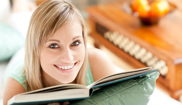 Happy woman lying on a sofa reading a book — Stock Photo, Image
