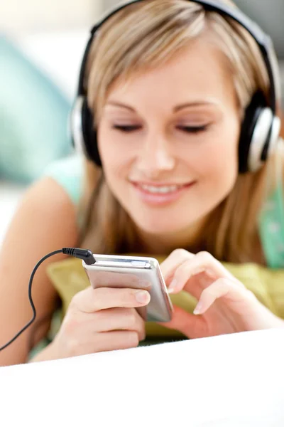 Attractive blond woman listening music lying on a sofa — Stock Photo, Image