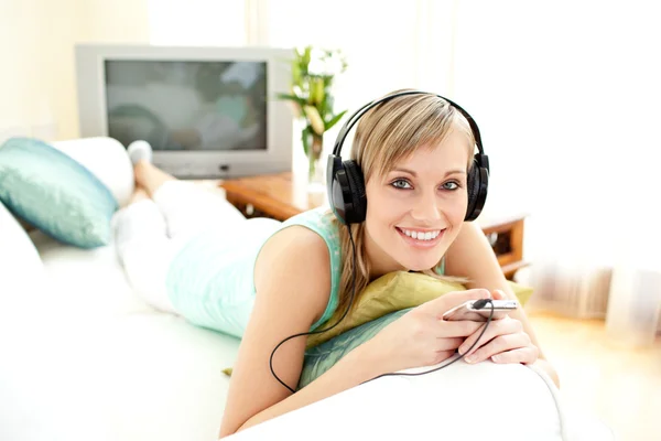 Mujer rubia alegre escuchando música tumbada en un sofá —  Fotos de Stock