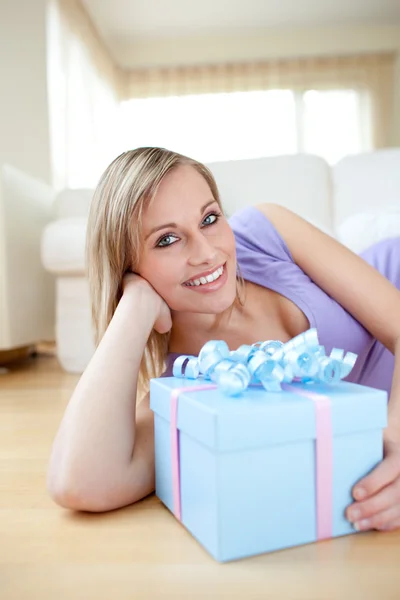 Bright woman holding a present lying on the floor — Stock Photo, Image