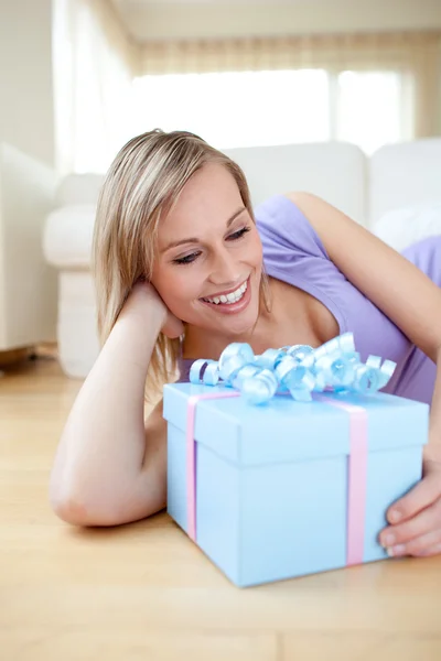 Mujer rubia feliz sosteniendo un regalo tirado en el suelo — Foto de Stock
